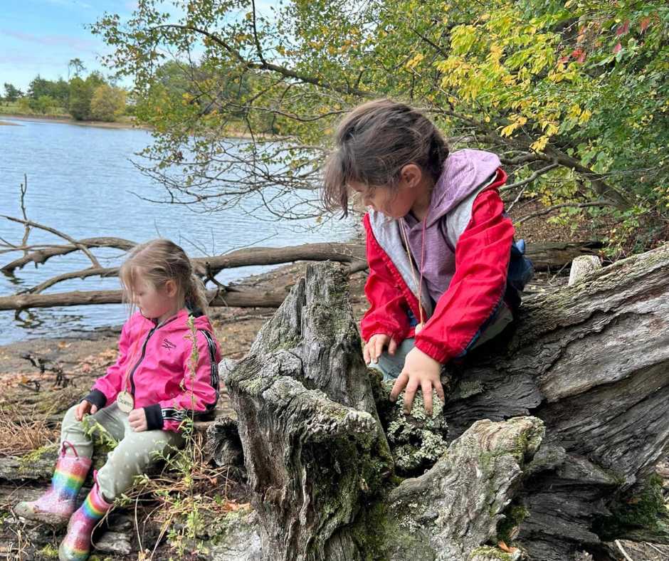 two girls on a log along the water 